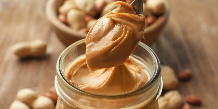 spoon and glass jar with creamy peanut butter on kitchen table, closeup